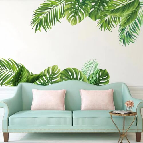 Autocollant murale feuilles tropicales au dessus d'un canapé vert pastel avec des coussins roses