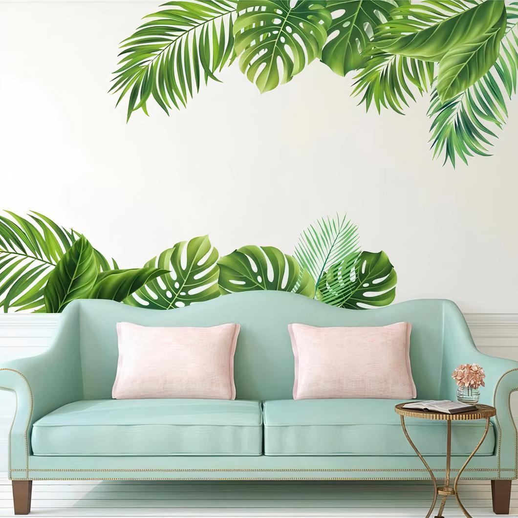 Autocollant murale feuilles tropicales au dessus d'un canapé vert pastel avec des coussins roses