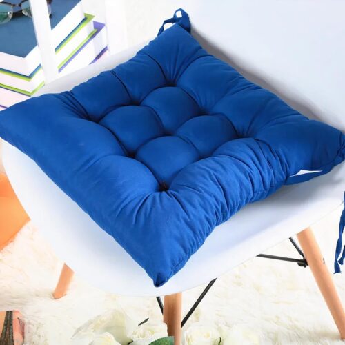 Photo d'un coussin de chaise bleu uni épais sur une chaise blanche à pieds obliques en bois, dans un décor clair
