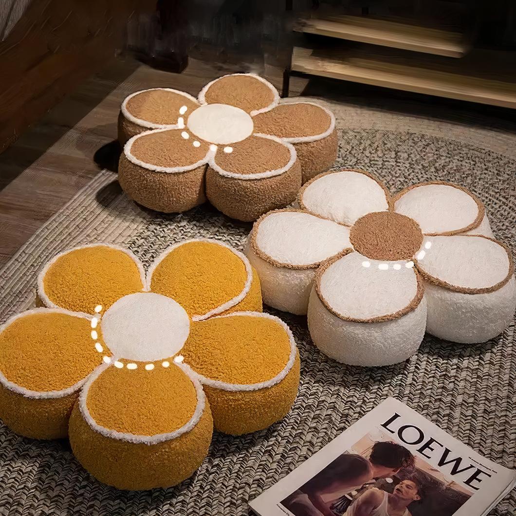 Photo de trois coussins de sol en forme de fleurs de trois couleurs différentes, un jaune, un blanc et un marron sur un tapis style jonc