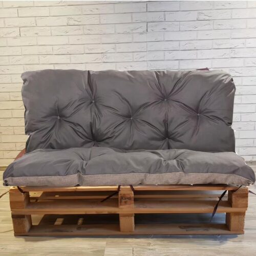 Photo d'un coussin gris moelleux et épais installé sur une double palette devant un mur de briques blanches style métro