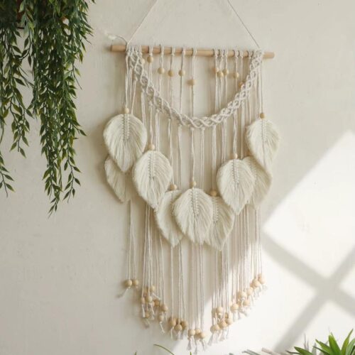 Décoration murale bohème en macramé avec motifs feuilles, sur un mur blanc.