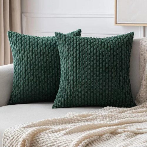 Photo de deux coussins carrés avec des housses vert foncé en tissu ciselé sur un canapé beige et plaid beige clair