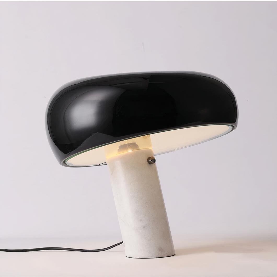 Photo d'une lampe à poser originale avec son pied en marbre blanc oblique et son abat-jour de couleur noire le tout sur un meuble blanc et un fond gris