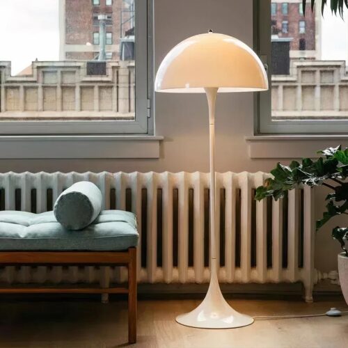 Photo d'une lampe de salon blanche design posée sur un sol en bois clair devant des fenêtres et un divan vert