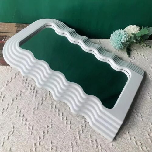 On voit un miroir vague contour blanc sur un tapis beige près de fleurs