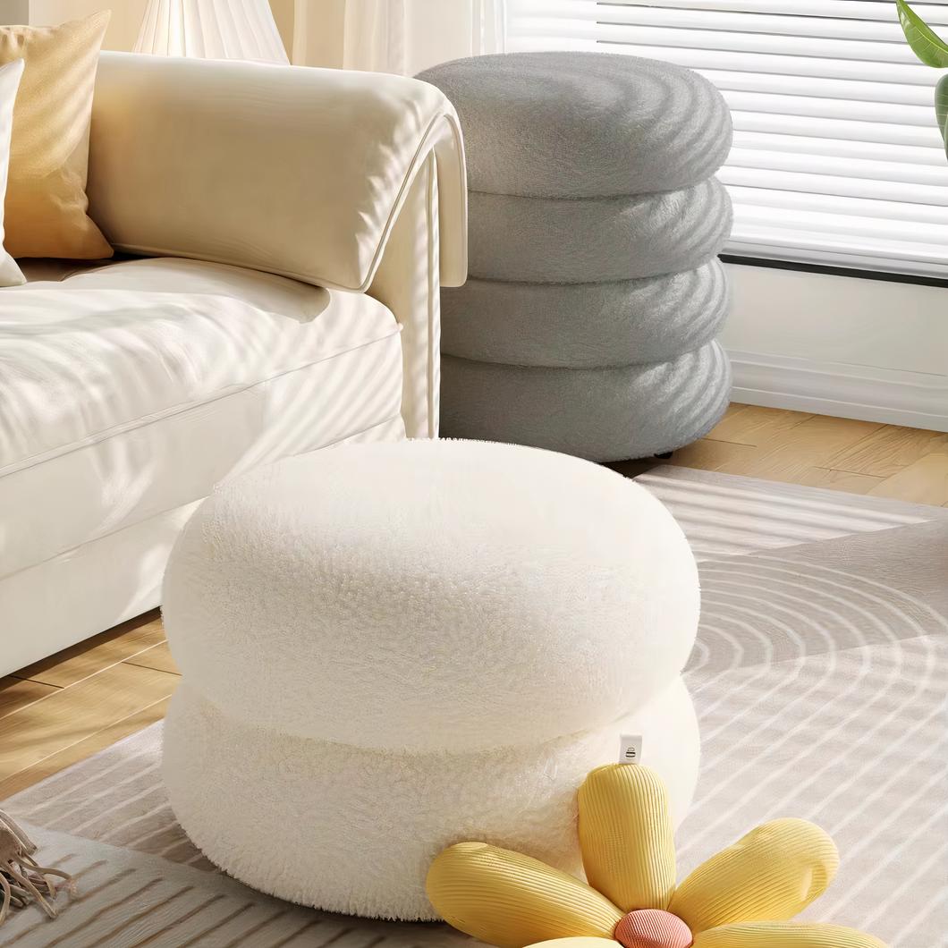 Photo d'un pouf design blanc à deux macarons et un gris en quatre macarons au second plan d'un salon au canapé blanc