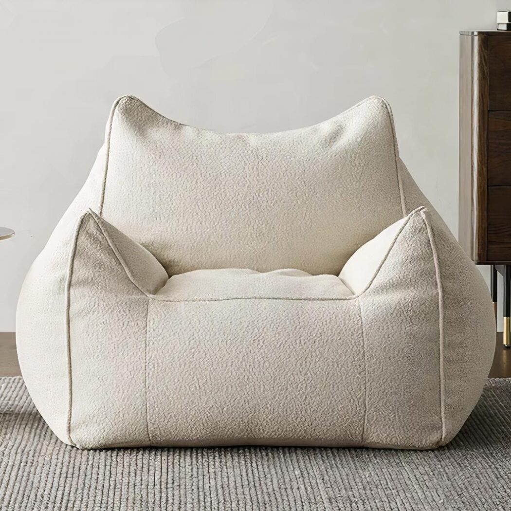 Photo d'un pouf fauteuil blanc avec accoudoirs et dossier installé sur une moquette grise devant un mur de salon beige