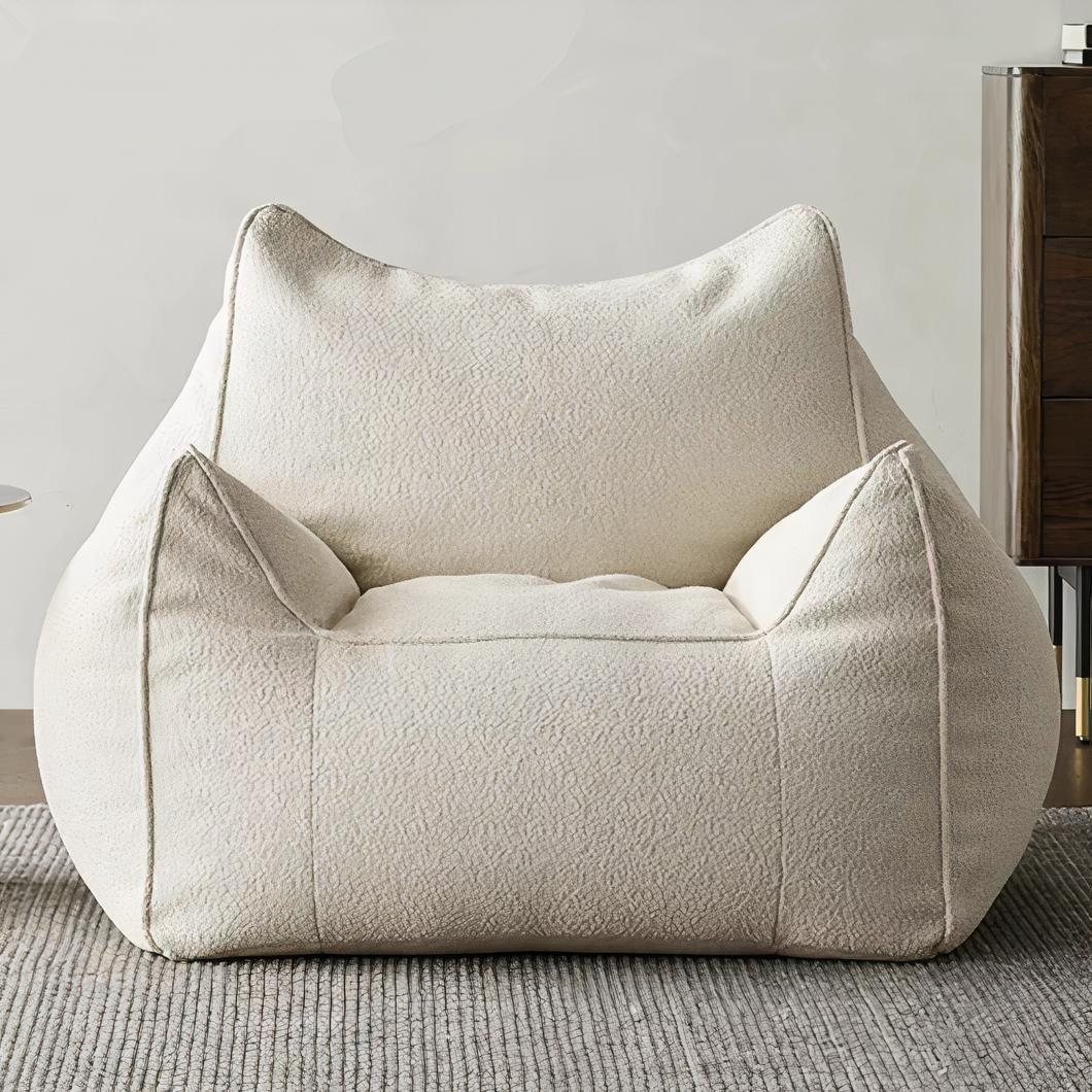 Photo d'un pouf fauteuil blanc avec accoudoirs et dossier installé sur une moquette grise devant un mur de salon beige