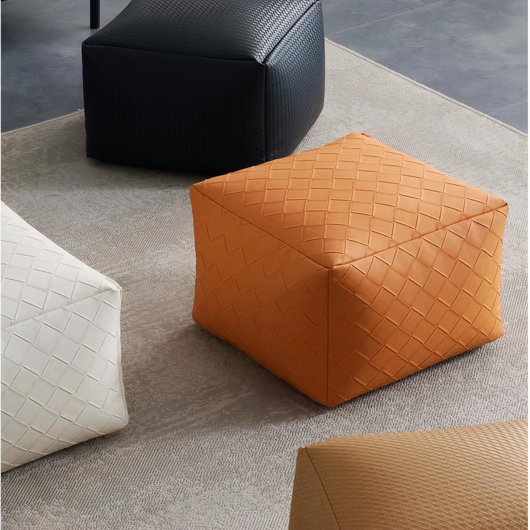 Photo de plusieurs poufs en simili cuir de couleurs noire blanche ou orange posés sur un tapis beige
