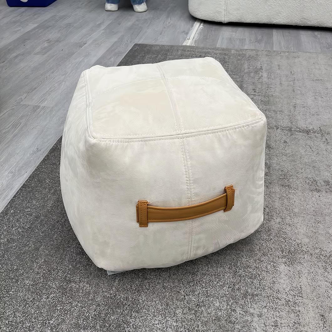 Photo d'un pouf tabouret blanc souple à poignée marron posé sur un sol gris