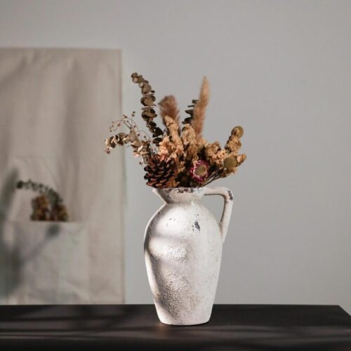 Vase blanc en terre cuite en forme de pichet avec des fleurs à l'intérieur.