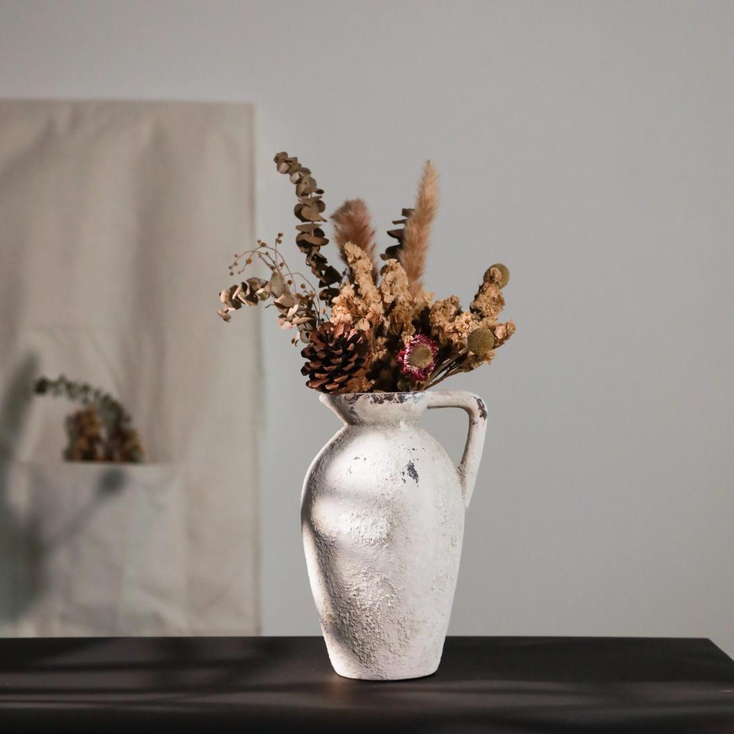 Vase blanc en terre cuite en forme de pichet avec des fleurs à l'intérieur.