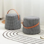 Photo de deux poufs design coniques pied de poule avec anse marron sur un tapis moderne blanc et marron devant un rideau blanc