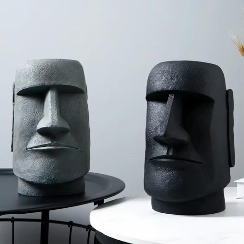 Photo représentant deux statuettes vases en têtes Moai l'une noire et l'autre grise sur des tables rondes, le tout sur fond gris