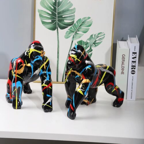 Photo représentant deux statuettes de gorilles noirs en position de marche bariolés de couleurs vives sur une étagère blanche devant des livres